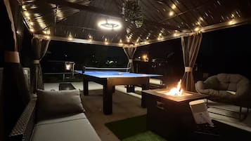 Uma área de estar externa com mesa de bilhar, assentos e lareira.