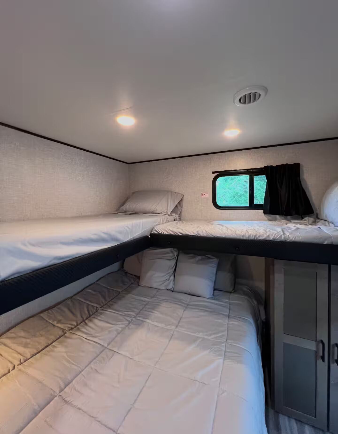 Interior compacto de autocaravana con dos literas, una ventana pequeña con cortinas y un armario.