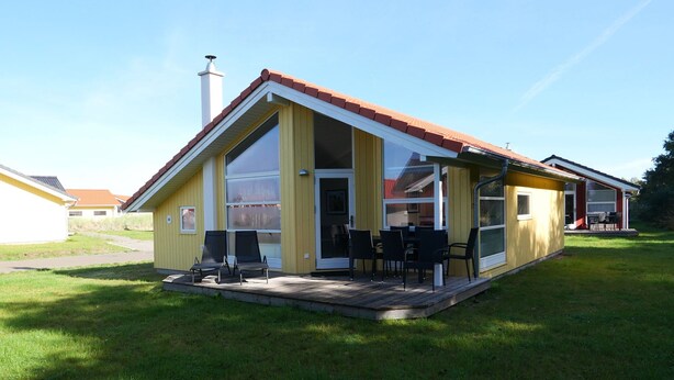 A yellow house with a red roof, a porch with chairs, and a large window. - Charming Seaside Haven Oasis fur 6 (Grossenbrode)