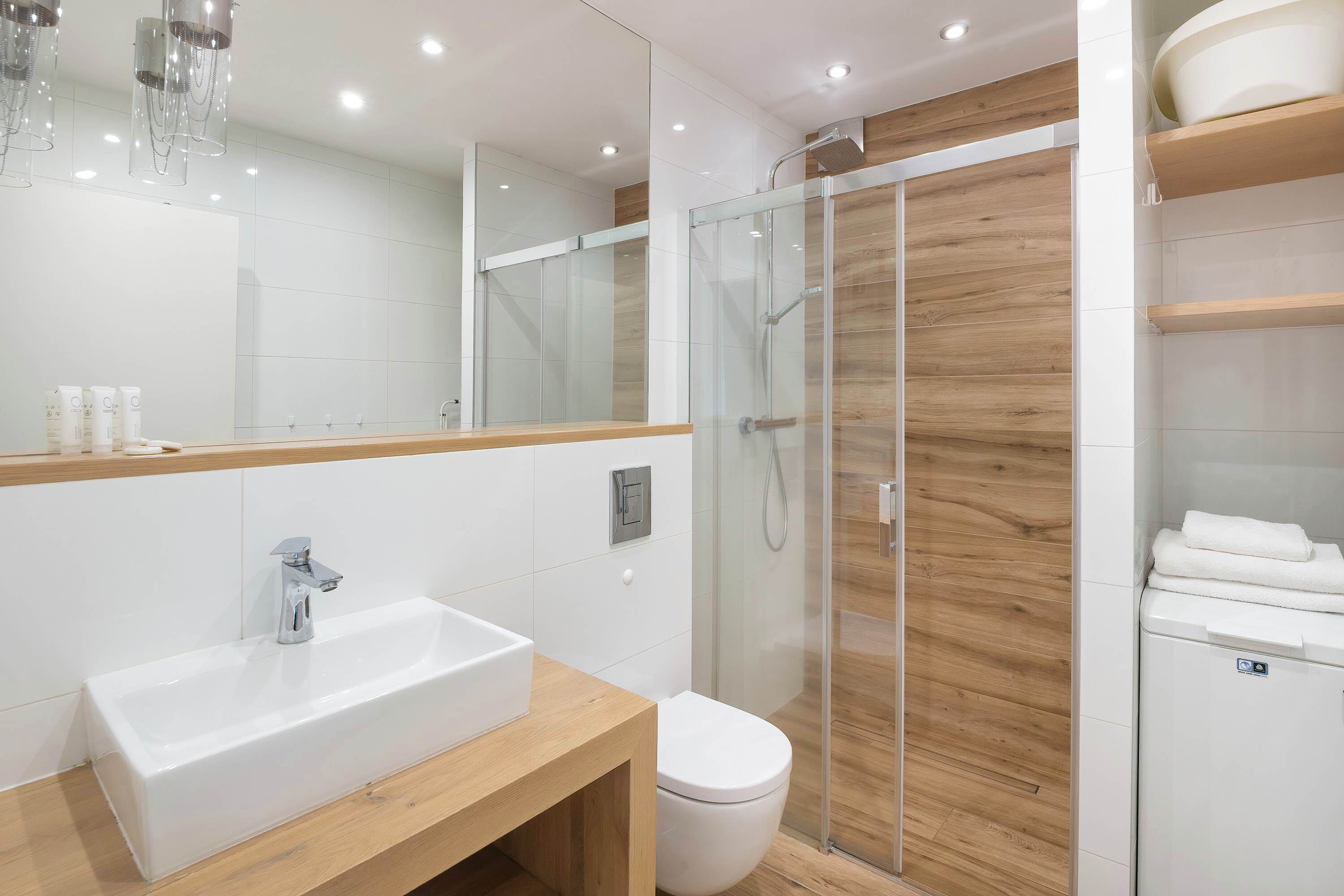 Et moderne badeværelse med en glasvægs brusekabine, en hvid vask og et toilet.