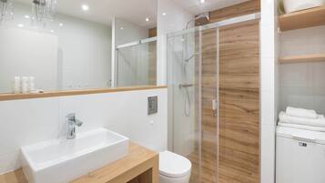 Et moderne badeværelse med en glasvægs brusekabine, en hvid vask og et toilet.