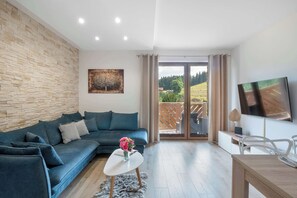 Un salon moderne avec un mur en pierre, un canapé bleu, une table basse avec un vase, un téléviseur à écran plat et une porte-fenêtre coulissante donnant sur un balcon.