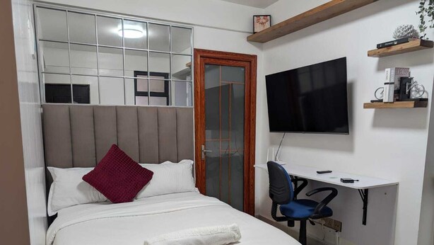 Un dormitorio con cama, escritorio, silla, televisor y ventana con persianas.