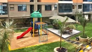 Un parque infantil con tobogán y estructuras de escalada, rodeado de césped y plantas en macetas.