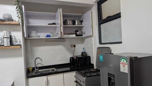 Cocina compacta con armarios blancos, encimera negra, estufa y refrigerador.