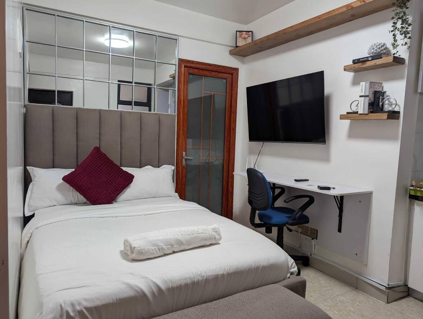 A bedroom with a bed, a desk, a chair, a television, and a door with a glass panel.