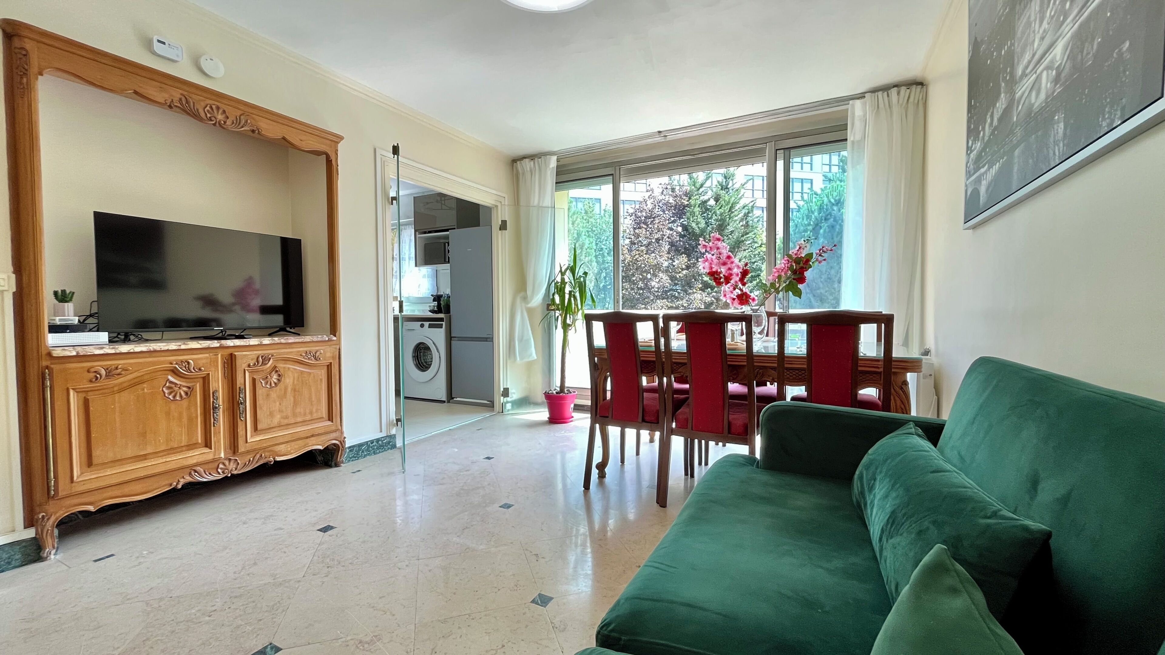 Een woonkamer met een televisie, een bank, een eethoek met tafel en stoelen, en een keuken in de achtergrond.