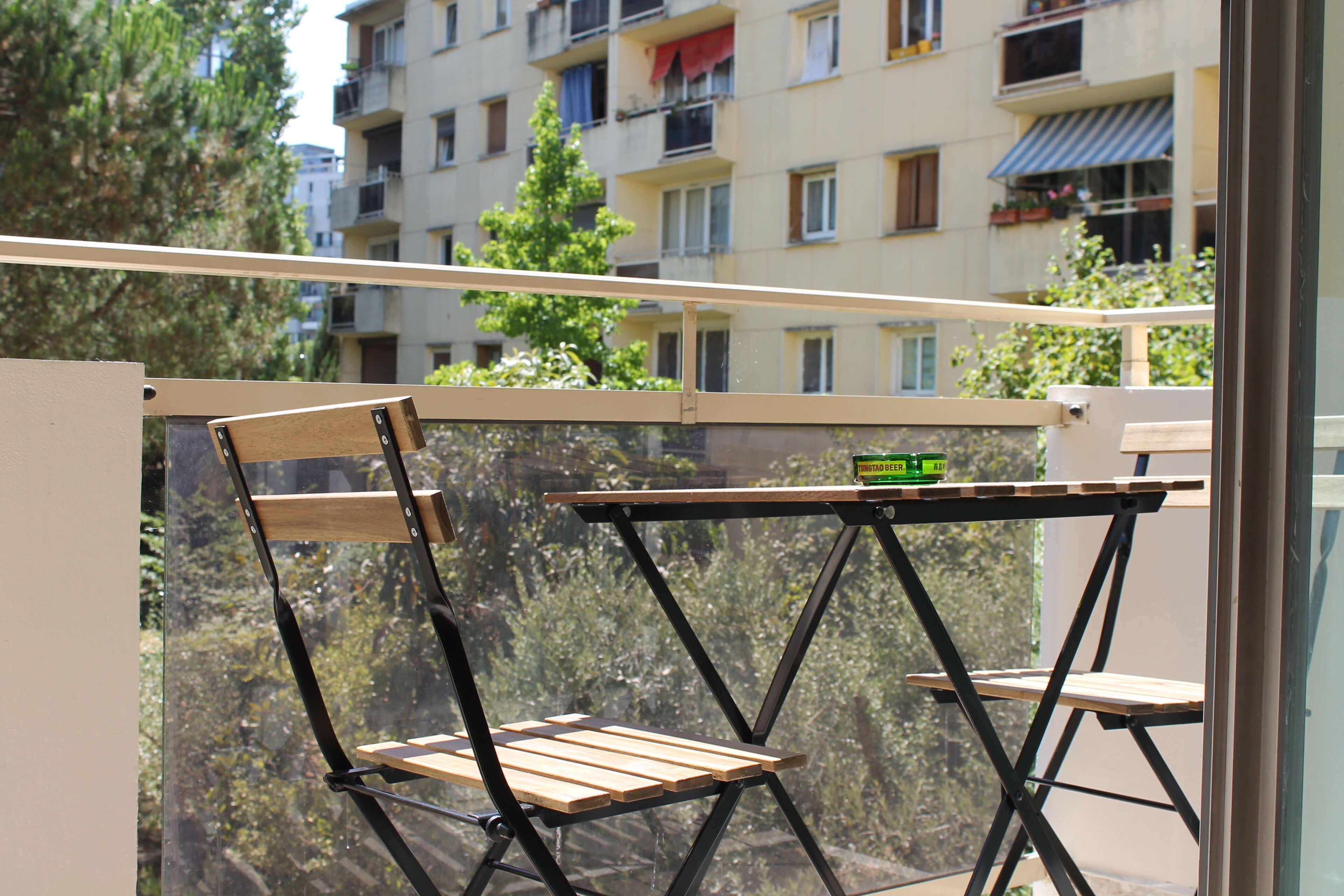 Un balcón con mesa y sillas de madera, con vistas a una zona residencial con edificios de varios pisos.