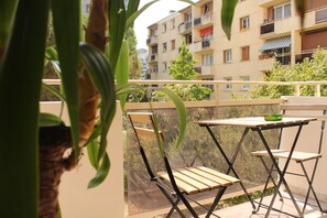 A balcony with a table and chairs, overlooking a building with multiple balconies. - Cozy Family Home in Paris: Comfort & Parking (Villejuif)
