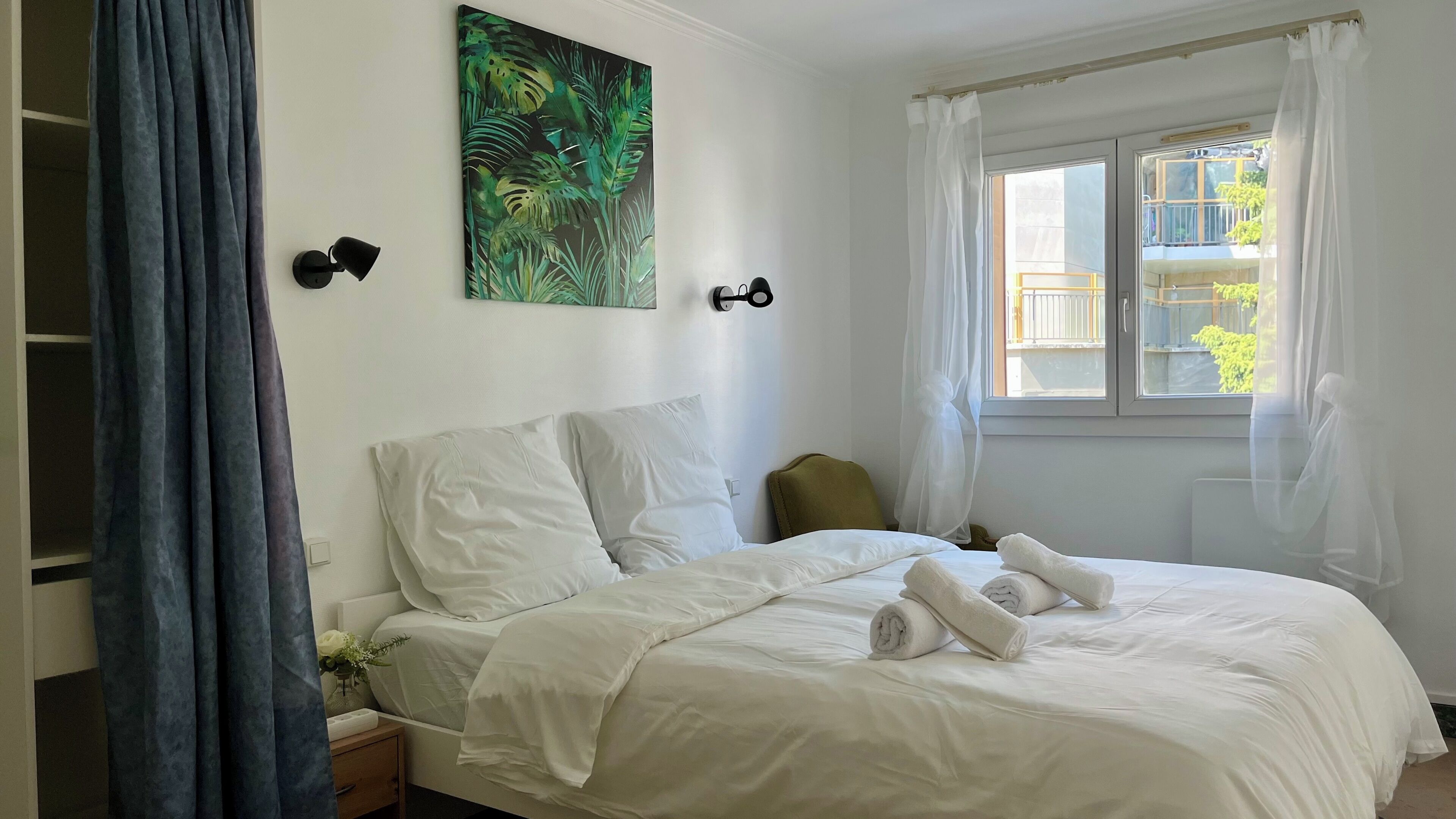 Ein Hotelzimmer mit einem Bett, einem Nachttisch, einem Gemälde und einem Fenster mit Vorhängen.