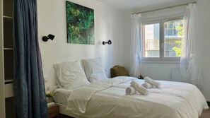 A hotel room with a bed, a nightstand, a painting, and a window with curtains. - Cozy Family Home in Paris: Comfort & Parking (Villejuif)
