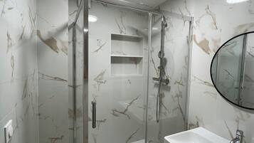 Une salle de bain moderne avec une douche à parois de verre, un lavabo blanc et un mur décoré d’un motif imitant le marbre.