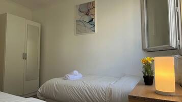 Ein Hotelzimmer mit Bett, Schrank, einem Gemälde, einer Topfpflanze und einer Nachttischlampe.