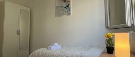 A hotel room with a bed, a wardrobe, a painting, a potted plant, and a bedside lamp.