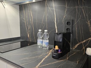 A kitchen counter with a black marble backsplash, two water bottles, a coffee maker, and a speaker. - Design studios in Pedregalejo - 4 guests (Málaga)