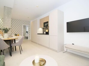 A modern kitchen with white cabinetry, a dining area with a round table and chairs, and a flat-screen TV mounted on the wall. - Design studios in Pedregalejo - 4 guests (Málaga)