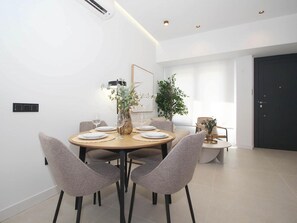A modern dining area with a round table, grey upholstered chairs, and a vase with greenery. - Cozy studio near beach - 4 guests (Málaga)