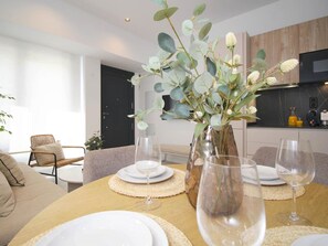 A dining area with a round table set for four, a vase with greenery, and a modern kitchen in the background. - Cozy studio near beach - 4 guests (Málaga)