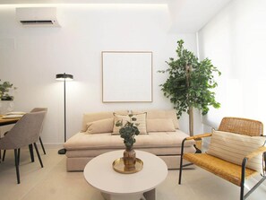 A modern living room with a sofa, a coffee table, a dining area with chairs, a floor lamp, and a large potted plant. - Cozy studio near beach - 4 guests (Málaga)