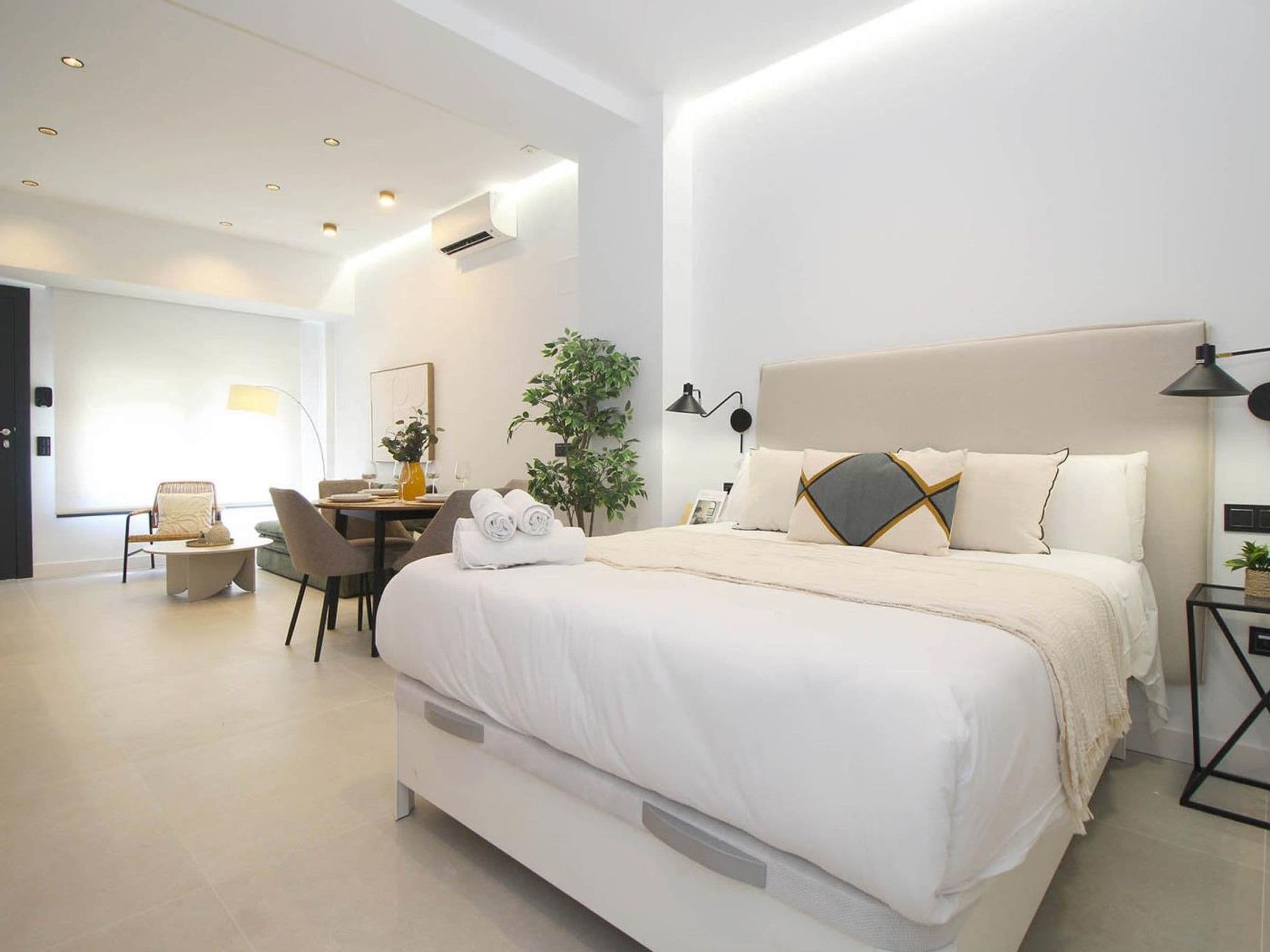A modern hotel room with a large bed, bedside tables, a desk, and chairs.