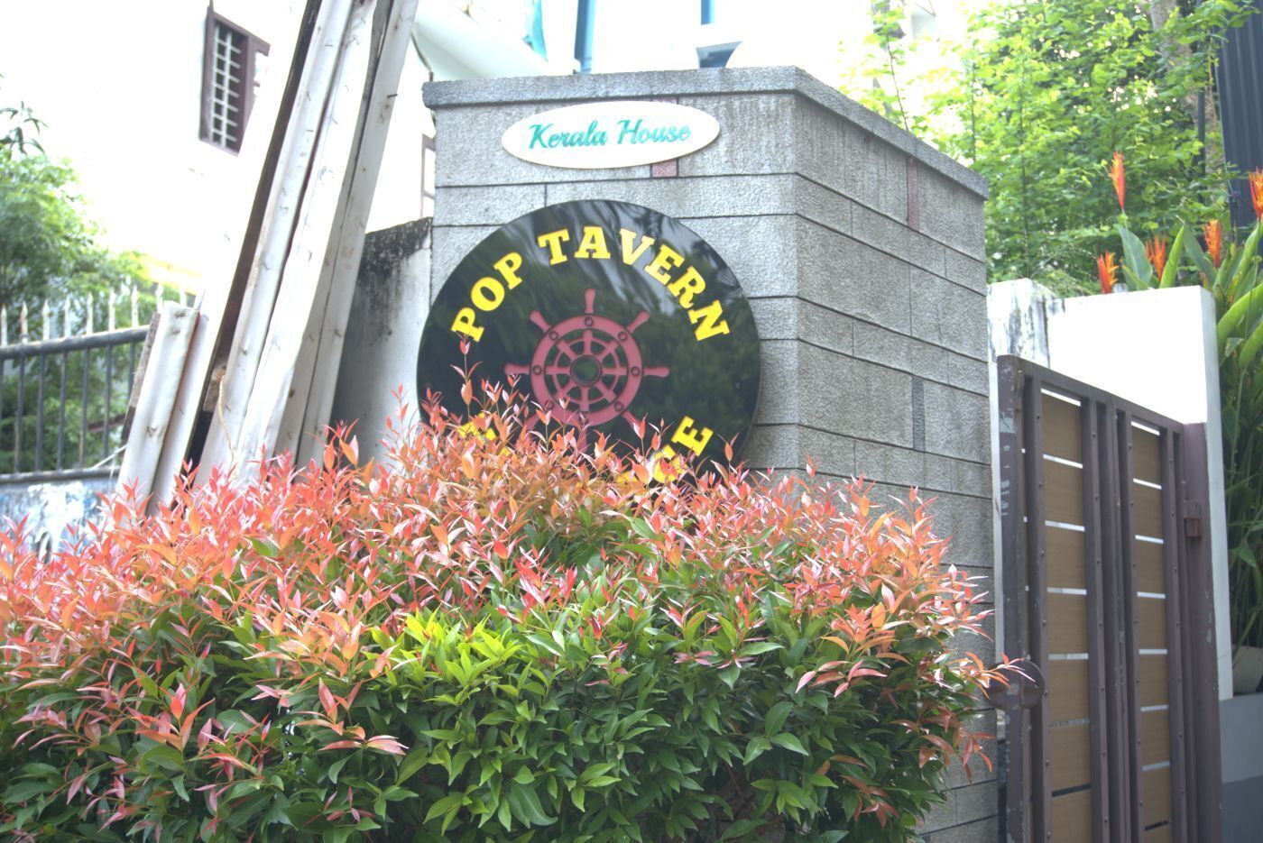 A sign for 'Pop Tavern' with a nautical wheel symbol, surrounded by foliage.