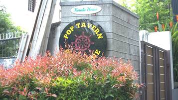 A sign for 'Pop Tavern' with a nautical wheel symbol, surrounded by foliage.
