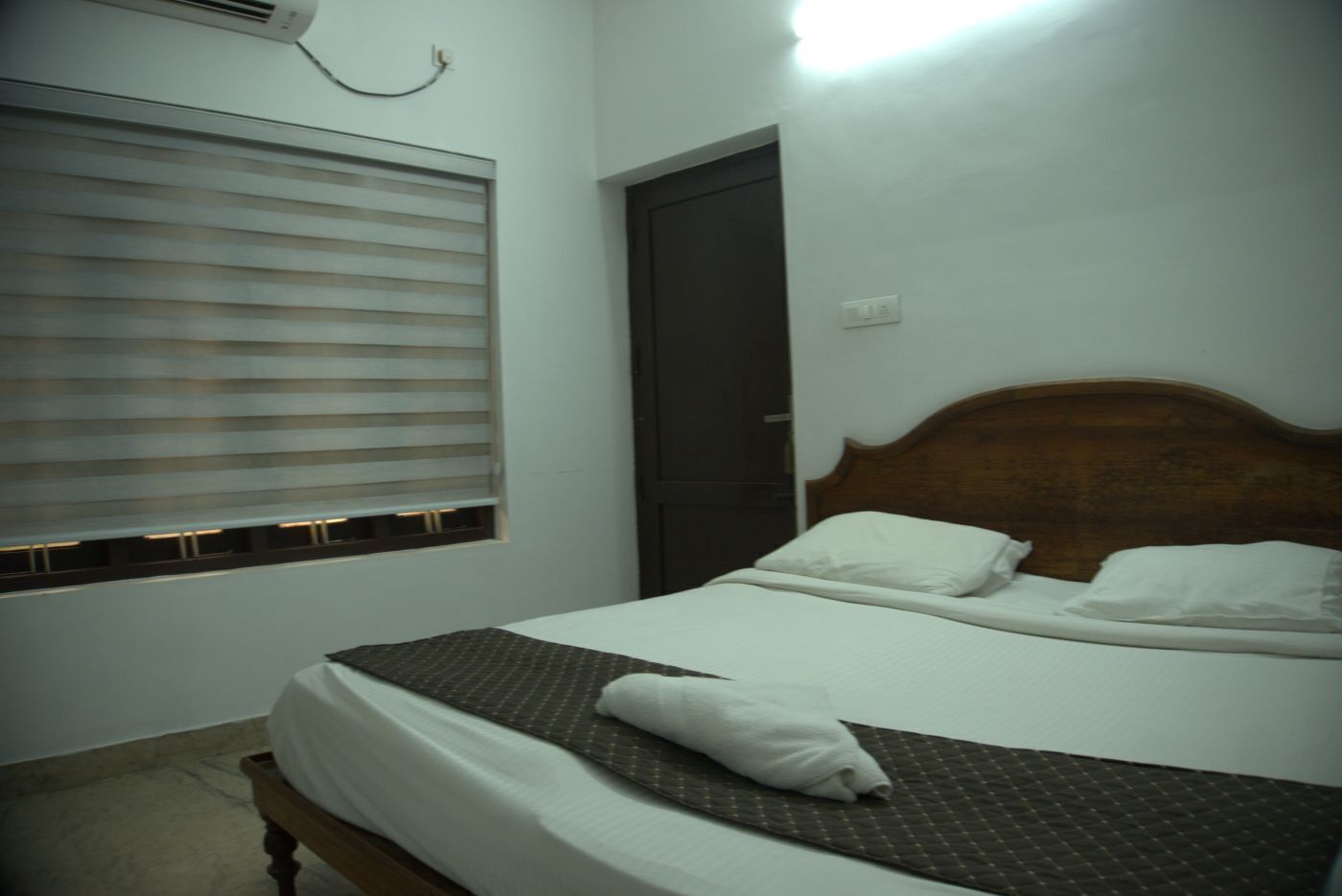 Una cama individual con cabecera de madera, una ventana con persianas y un equipo de aire acondicionado instalado en la pared.