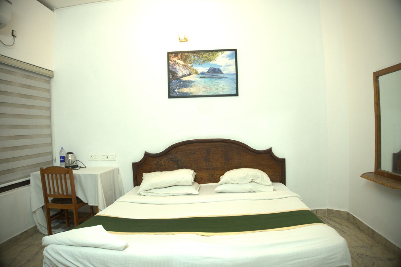 A hotel room with a bed, a chair, a small table, and a painting on the wall.