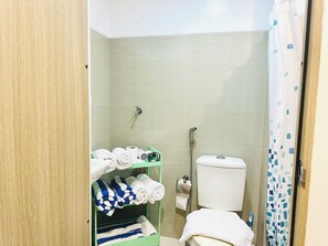 A bathroom with a toilet, a shower, and a shelf with towels. - Stylish 2-Bed Family Suite in Mall of Asia near Airpot/NAIA/Solaire/Pasay (Pasay City)