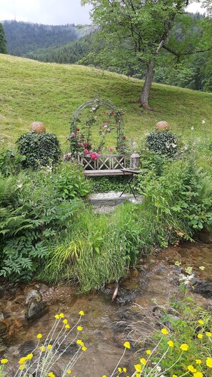 A garden with a wooden bench, a metal archway, and a small stream.