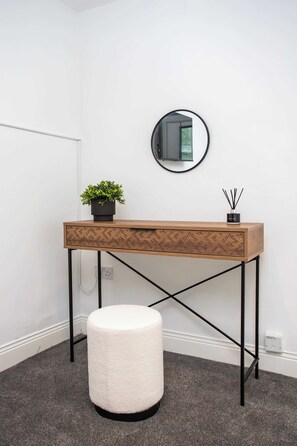 A room with a wooden desk, a round mirror, a potted plant, a small stool, and a wall socket. - Vacant Nests The Esplinade City Centre Wifi (Sunderland)