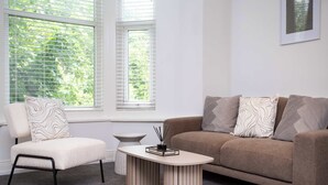 A modern living room with a beige sofa, a matching armchair, and a small round table with a candle holder. - Vacant Nests The Esplinade City Centre Wifi (Sunderland)