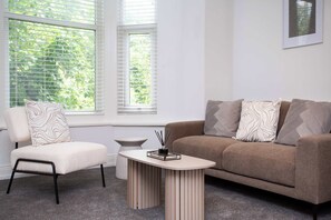 A modern living room with a beige sofa, a matching armchair, and a small round table with a candle holder. - Vacant Nests The Esplinade City Centre Wifi (Sunderland)