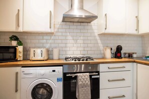 A compact kitchen with a washing machine, a gas stove, and a toaster. - Vacant Nests The Esplinade City Centre Wifi (Sunderland)