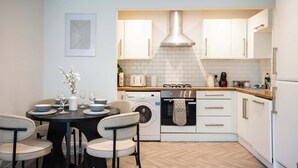 A compact kitchen with a central island, a washing machine, and a built-in oven. - Vacant Nests The Esplinade City Centre Wifi (Sunderland)