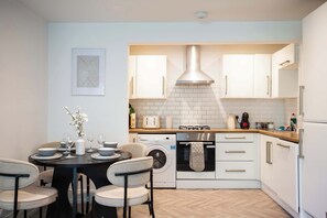 A compact kitchen with a central island, a washing machine, and a built-in oven. - Vacant Nests The Esplinade City Centre Wifi (Sunderland)