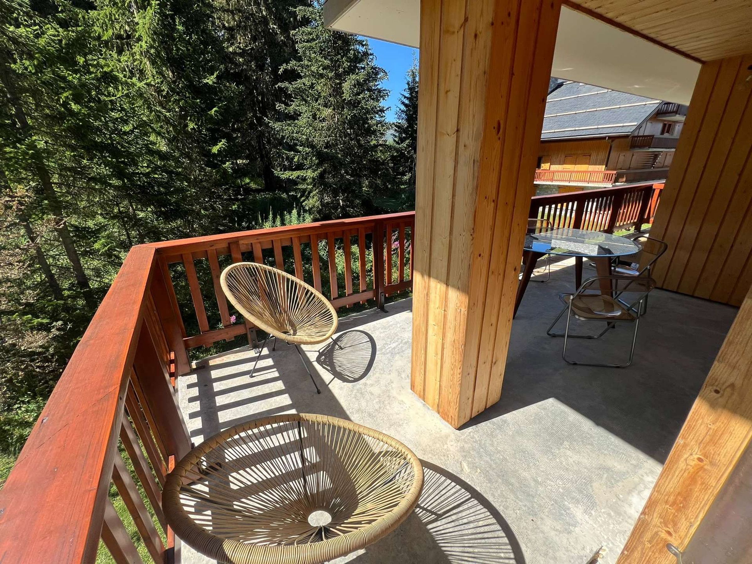 A wooden balcony with two wicker chairs and a table, overlooking a forested area.