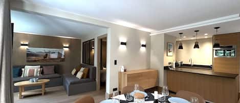 A modern dining area with a table set for four, a sofa, and a kitchen in the background.
