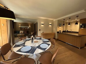 A dining area with a round table set for four, surrounded by brown chairs, in a modern kitchen with wooden cabinets and pendant lighting. - Family apartment near slopes - 8 guests (Méribel)