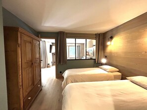 A hotel room with two beds, a wooden wardrobe, a window with curtains, and a wall-mounted light fixture. - Family apartment near slopes - 8 guests (Méribel)