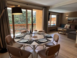 A dining area with a round table set for four, surrounded by chairs, with a view of a wooden deck and trees outside. - Family apartment near slopes - 8 guests (Méribel)