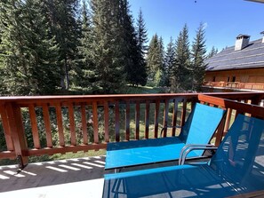 A wooden deck with a blue chair and a view of a forested area. - Family apartment near slopes - 8 guests (Méribel)