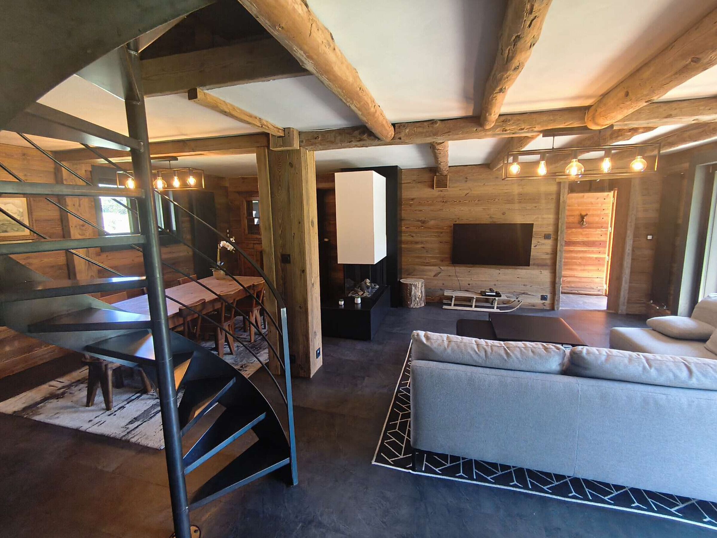 Un intérieur moderne comprenant un escalier, un canapé, un coin repas et un téléviseur à écran plat fixé à un mur en bois.