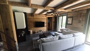 Ein modernes Wohnzimmer mit einer Couch, einem flachbildfernseher an der Wand und einer Holzbalkendecke.