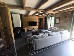 A modern living room with a sofa, a flat-screen TV mounted on the wall, and a wooden ceiling structure. - Spacious apartment near center - 8 guests (Arâches-la-Frasse)