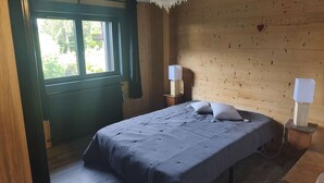Ein Schlafzimmer mit Holzwand, einem Bett mit grauer Bettdecke, zwei Nachttischen mit Lampen und einem Fenster mit Vorhängen.