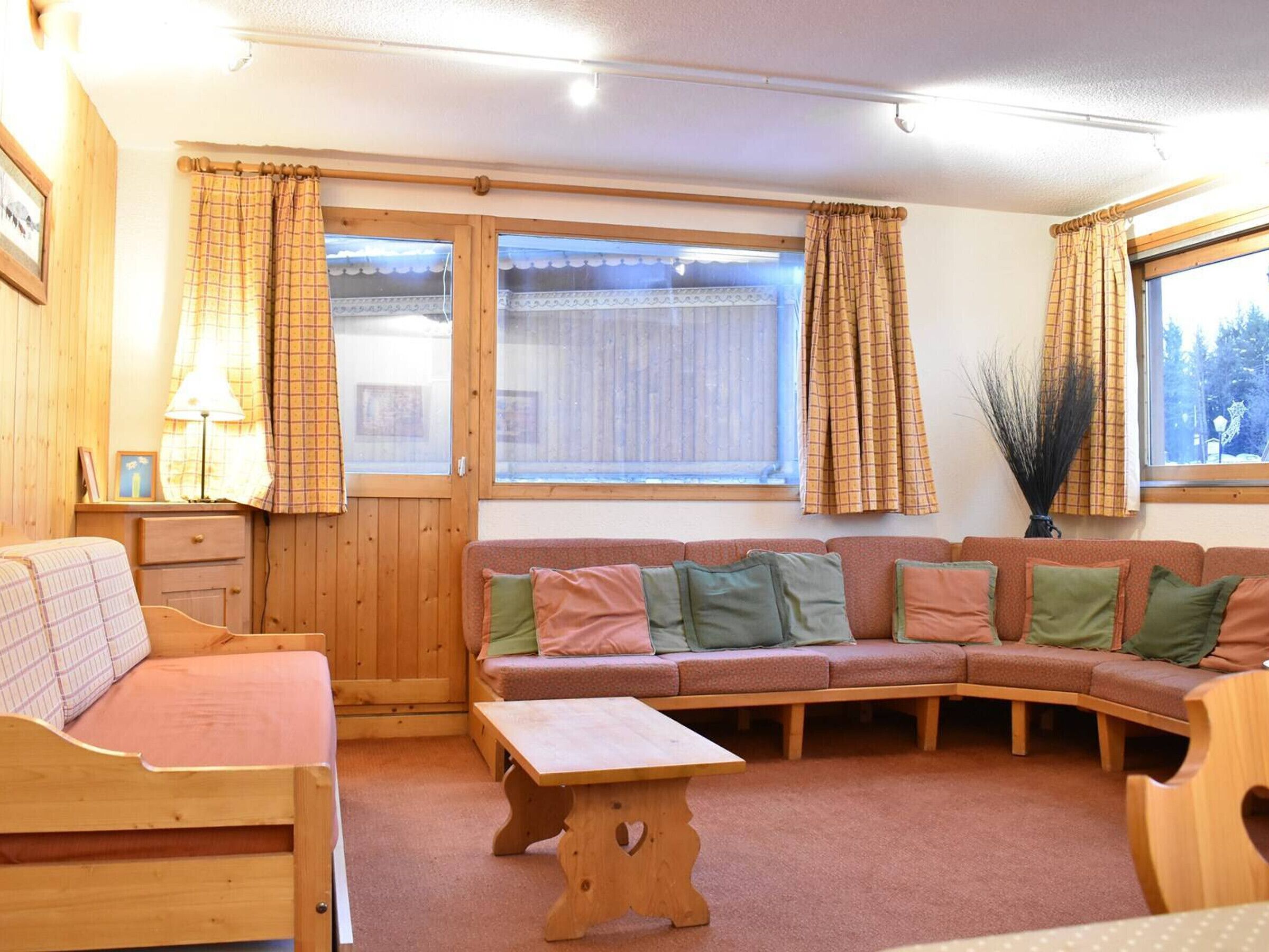 Una stanza accogliente con una panca in legno, un divano con cuscini, un tavolino e una finestra con tende.