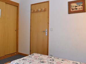A room with two wooden doors, one with a handle and the other with a lock. There's a bed with a floral-patterned bedspread, a small picture frame on the wall, and a light switch. - Spacious apartment, mountain view - 6 guests (Méribel)
