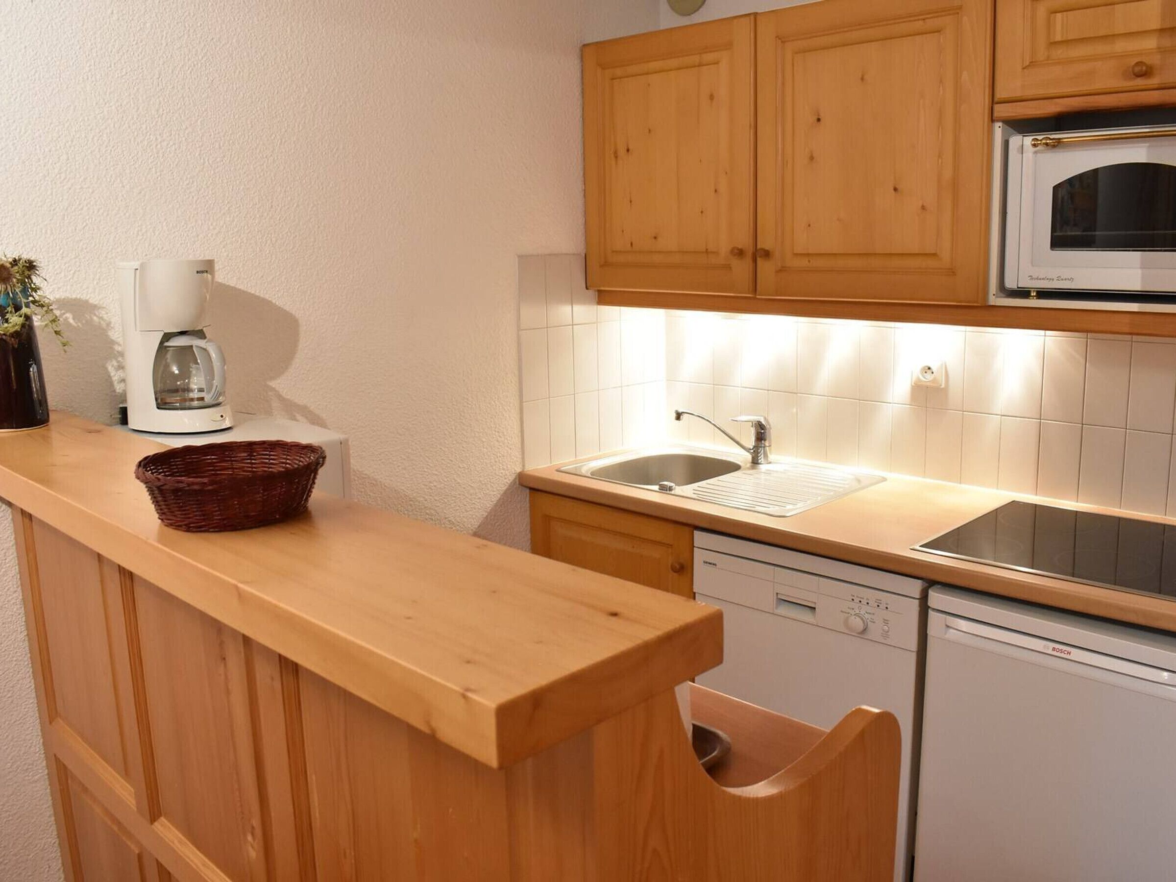 A kitchen with wooden cabinets, a microwave, a Bosch dishwasher, and a coffee maker.