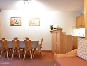 Ein Zimmer mit Esstisch, Stühlen, einer Couch, einer Küchenzeile und zwei gerahmten Bildern an der Wand.